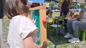 Una nena pinta mentre al fons, altres infants juguen