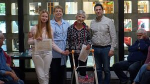 Una de les parelles, formada per una adolescent i una dona gran, reben el diploma de mans de l'alcalde i de la regidora de Gent Gran. Estan dretes.