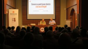 Una sala plena de gent, escoltant dos homes que parlen a l'escenari