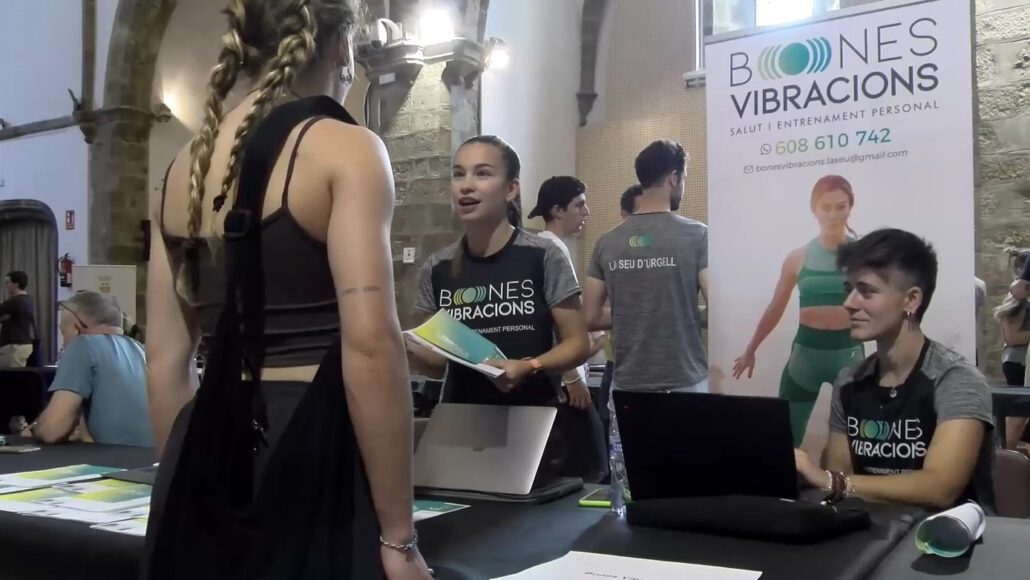 Una jove amb roba esportiva parlant amb una noia en un estand de temàtica esportiva