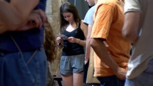 Una jove, amb roba esportiva, llegint un fulletó envoltada de gent